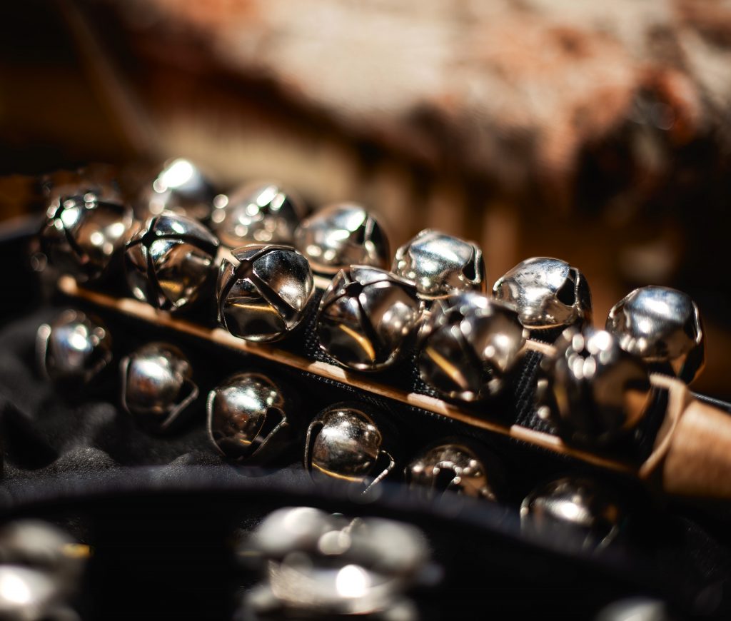 A cluster of shiny sleigh bells on a wooden handle.