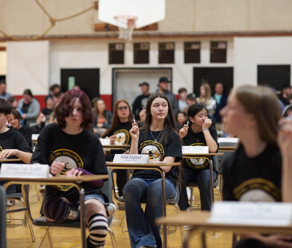 A student raises their hand during the 50th Annual Tuolumne County Spelling Bee, listening attentively.